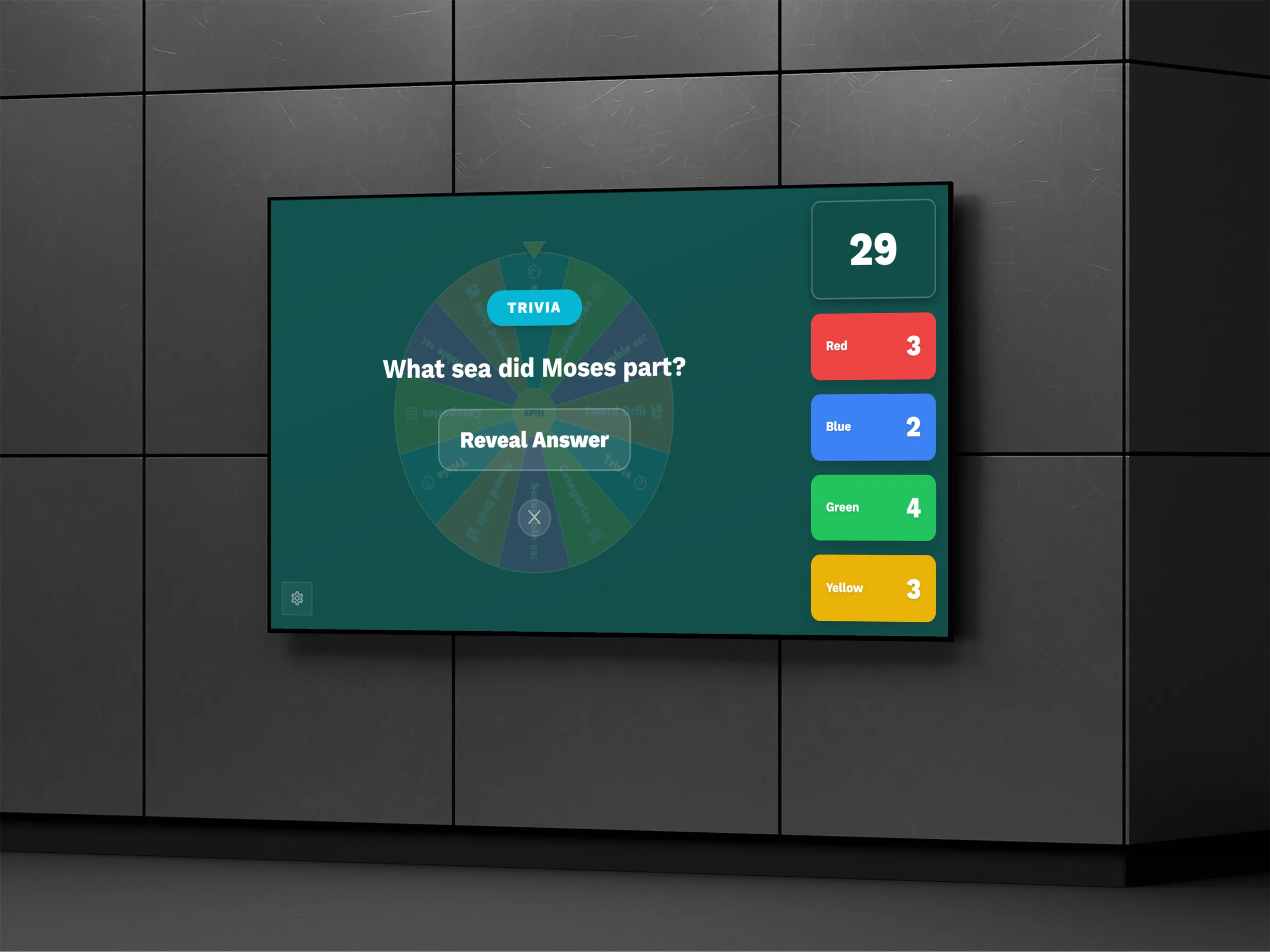 A wall-mounted television running a Signal Fire Games trivia round on a teal screen, asking which sea Moses parted, with a Reveal Answer button and a team scoreboard showing Red, Blue, Green, and Yellow scores.